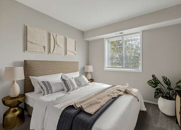A bedroom with a bed, two lamps, a window, and a plant.