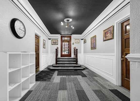 A hallway with a clock on the wall and a staircase in the background at Pleasant Oak Apartments, Oak Park
