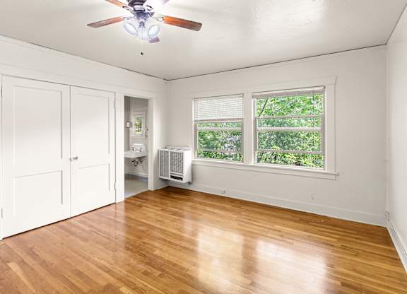 A room with a ceiling fan and a window with a view of trees.