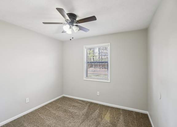 A room with a ceiling fan and a window with blinds.