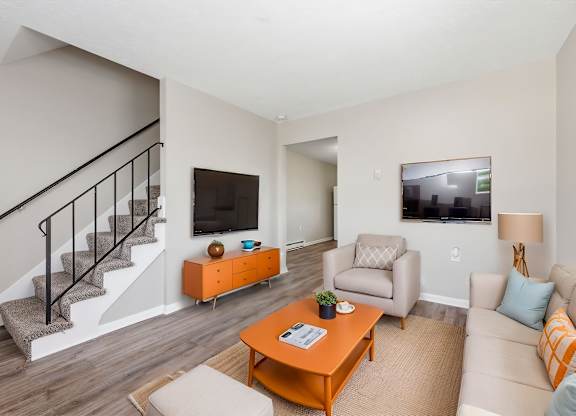 A living room with a staircase, a couch, a chair, a coffee table, and a television.
