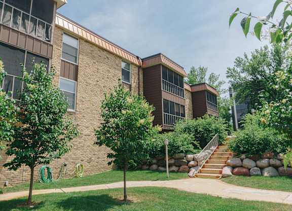 A building with a brown brick exterior and a green lawn in front at Astor Place of Edina Apartments , Edina, MN, 55435