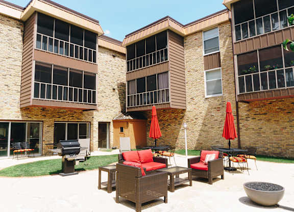 A patio area with furniture and umbrellas in front of a brick building at Astor Place of Edina Apartments , Edina, Minnesota
