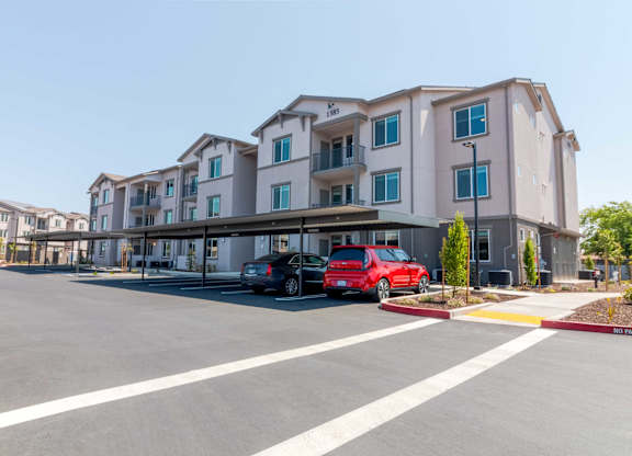 A red car is parked in front of a multi-story apartment building.