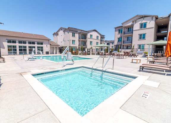 A hot tub with a swimming pool and apartment buildings in the back