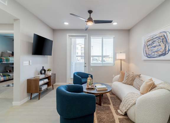 A living room with a blue armchair, a white sofa, and a ceiling fan.