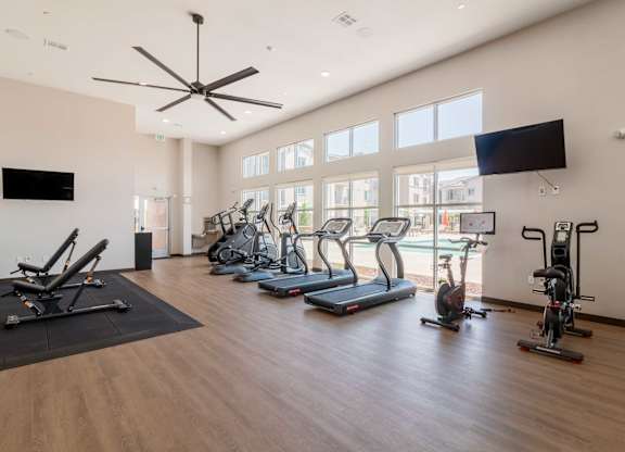 A spacious gym with a variety of exercise equipment and a ceiling fan.