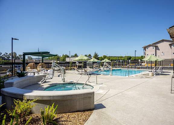 A large outdoor swimming pool with a hot tub and lounge chairs.