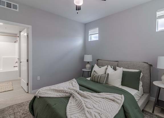 A bedroom with a bed covered in a green blanket and pillows.