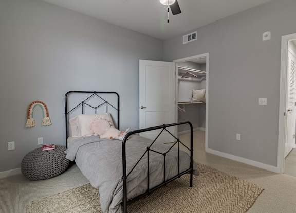 A bedroom with a bed, a rug, a ceiling fan, and a door leading to another room.