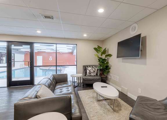 A living room with a brown leather couch, a white coffee table, and a flat screen TV mounted on the wall.