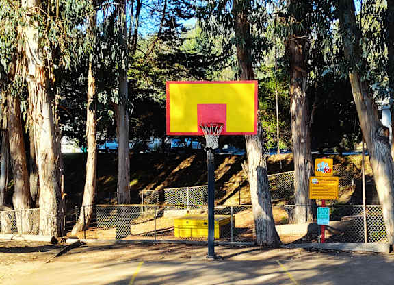 A basketball court surrounded by trees with a yellow hoop at Salinas Sunset Apartments, Salinas