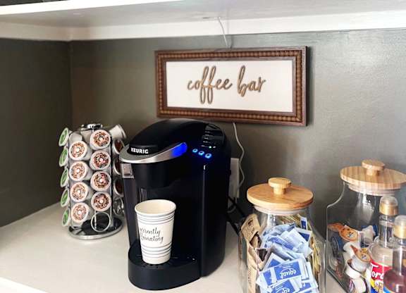 a coffee bar in a kitchen with a coffee maker and coffee cups on a shelf