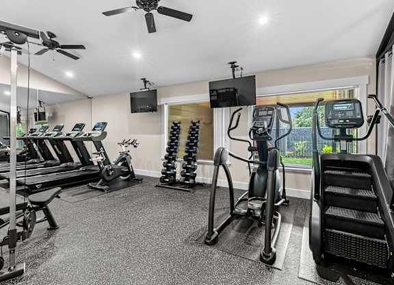 A spacious gym with treadmills, elliptical machines, and a fan.