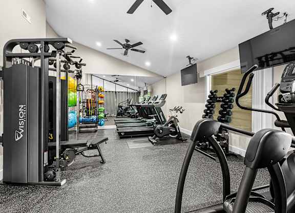 A gym with a variety of equipment including treadmills, weights, and a television.