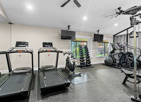 A gym with treadmills, elliptical machines, and a ceiling fan.