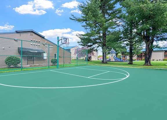 A basketball court is surrounded by a green fence.
