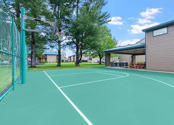 A tennis court with a green fence and a building in the background.