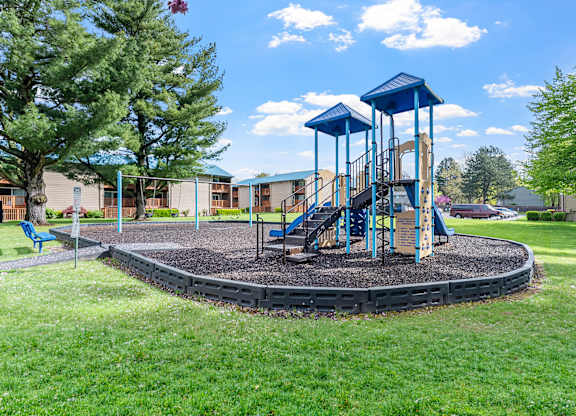 A playground with a blue swing set and a round sandbox.