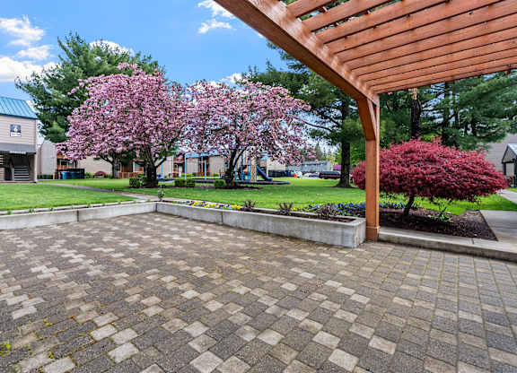 A patio with a wooden pergola and a brick patterned floor.