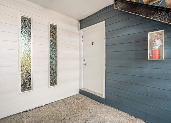 A white door is in a room with white siding and a fire extinguisher is on the wall.