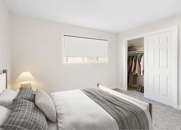 A bedroom with a bed, pillows, a lamp, and a closet.