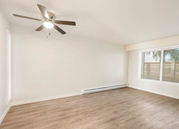 A room with a ceiling fan and light, hardwood floors, and a window with blinds.