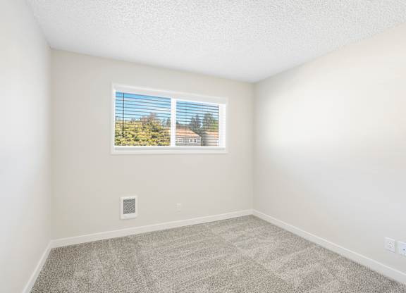 A room with a window showing a view of trees and a building outside.