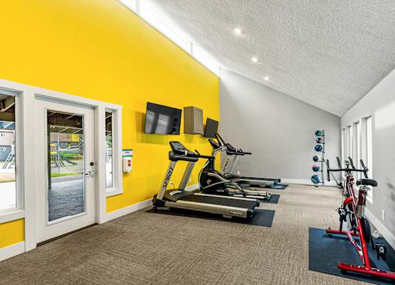 A bright yellow wall with a treadmill and exercise equipment in a room.