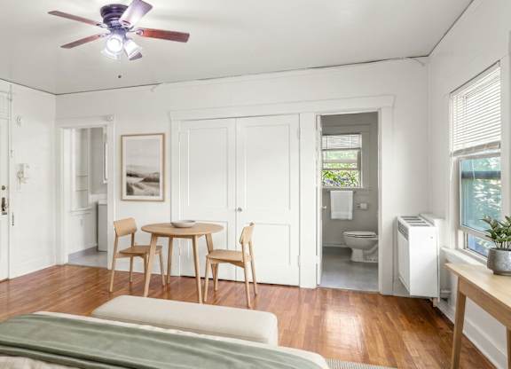 A bedroom with a bed, a table and chairs, and a ceiling fan.
