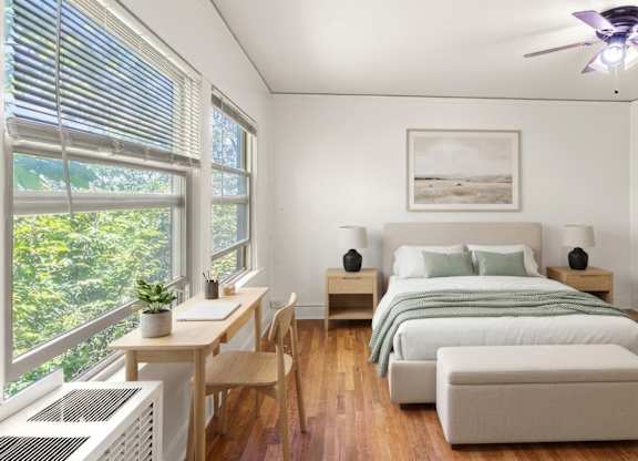 A bedroom with a bed, a table, and a ceiling fan.