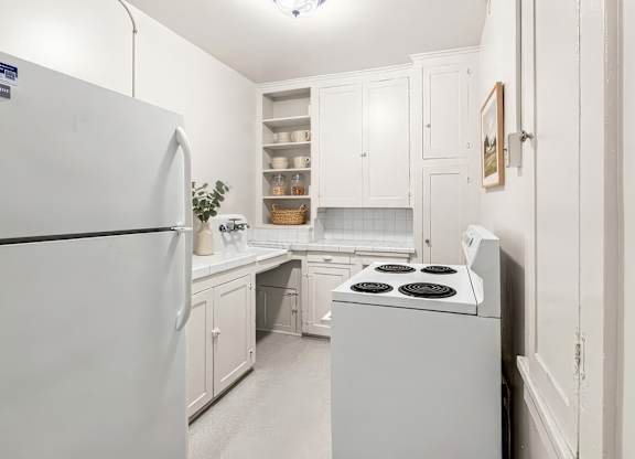 A white kitchen with a refrigerator, stove, and cabinets.