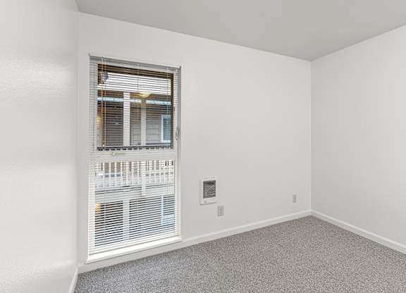 A room with a window and a thermostat on the wall.
