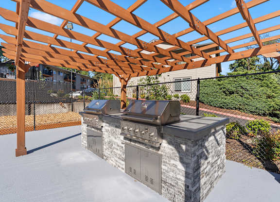 A wooden pergola is over a stone and metal grill.