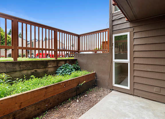 A small patio with a wooden railing and a glass door.at East Wind, Gresham, OR 97030
