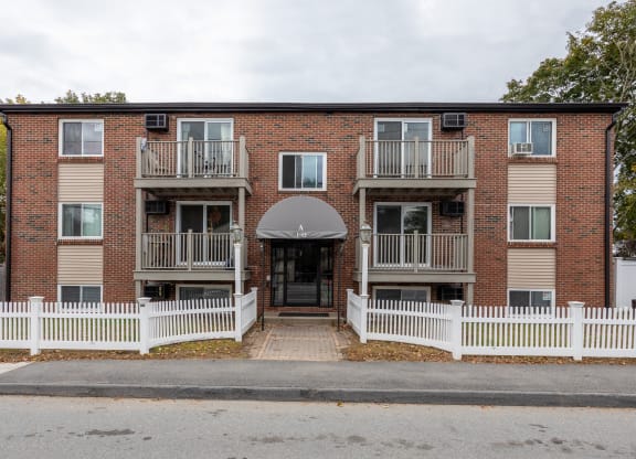 the front of a brick apartment building with a white fence at Flats at Merrill Pond, Massachusetts