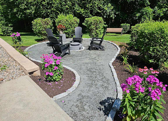 A garden with a circular concrete table surrounded by chairs and flowers.
