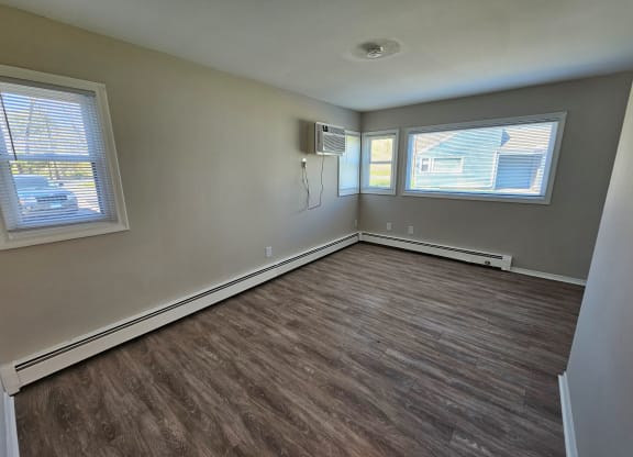 an empty bedroom with wood flooring and two windows