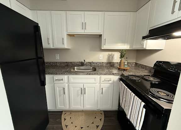A black refrigerator stands in a kitchen with white cabinets.