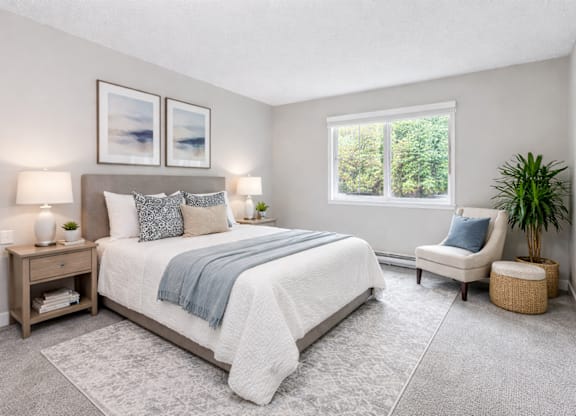 A bedroom with a large bed, a chair, and a potted plant.