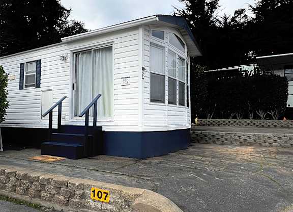 A small white house with a blue staircase and a number 107 on the ground.