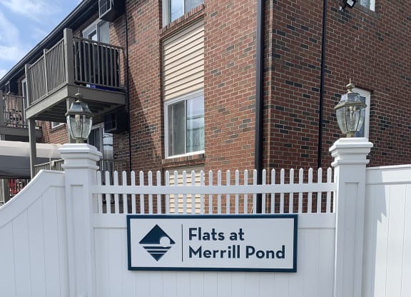 a white fence with a sign that reads Flats at Flats at Merrill Pond, Worcester, MA 01607