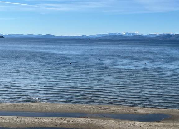 A calm body of water with mountains in the distance and a clear sky.