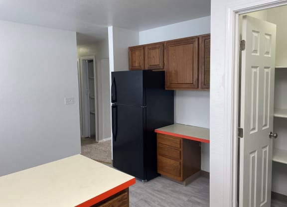 an empty kitchen with a black refrigerator and wooden cabinets