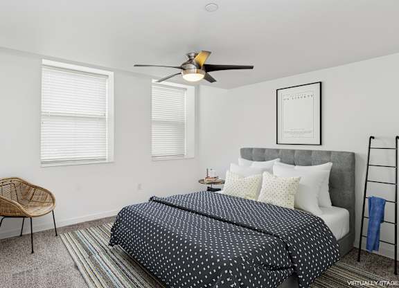 A bedroom with a bed, chair, and a ceiling fan.