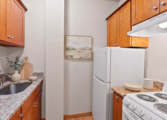 A kitchen with a white refrigerator, stove, and wooden cabinets.