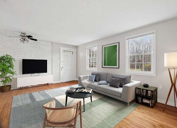 A living room with a grey couch, a black coffee table, a white television, a ceiling fan, and a green rug.