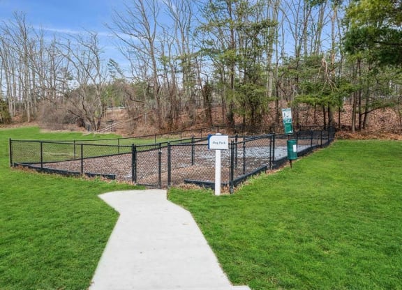 a fenced in dog park with green grass and trees at ReNew Odenton, Odenton