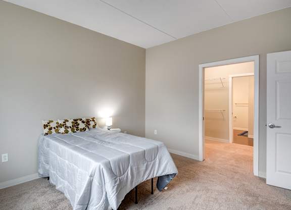 A bedroom with a bed, a lamp, and a carpeted floor.