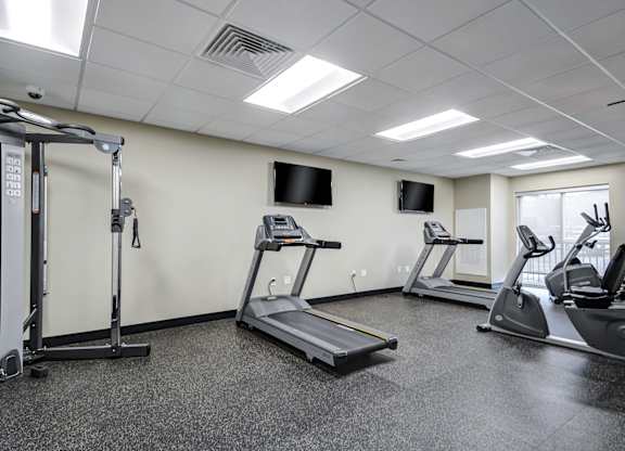 A gym with treadmills, elliptical machines, and a television.